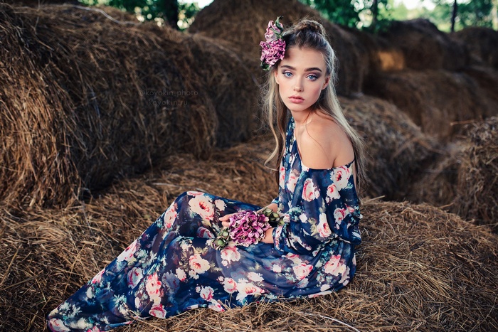 Woman with flower in hair sitting on haystacks