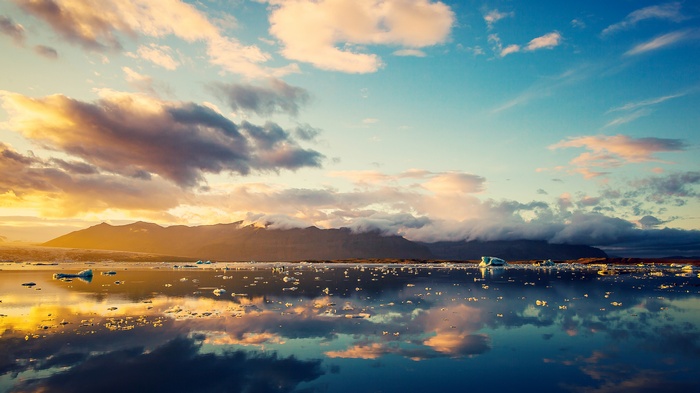 Icebergs floating in a lake with mountains and clouds at sunset