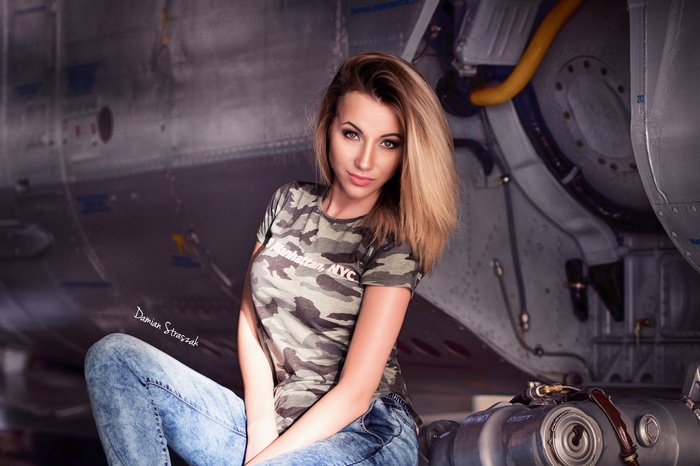 Woman in camouflage T-shirt and jeans sitting near an airplane