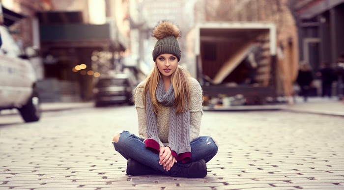 Woman in winter clothes sitting on cobblestone street