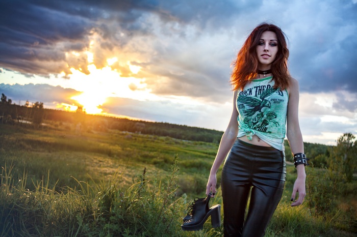 Woman in leather leggings holding shoes at sunset