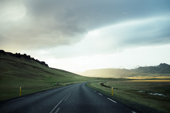 Road through a green landscape under a cloudy sky