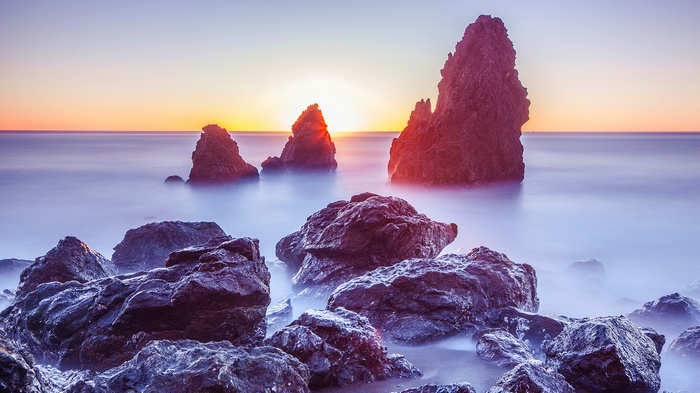 Rocks in the ocean at sunset with mist