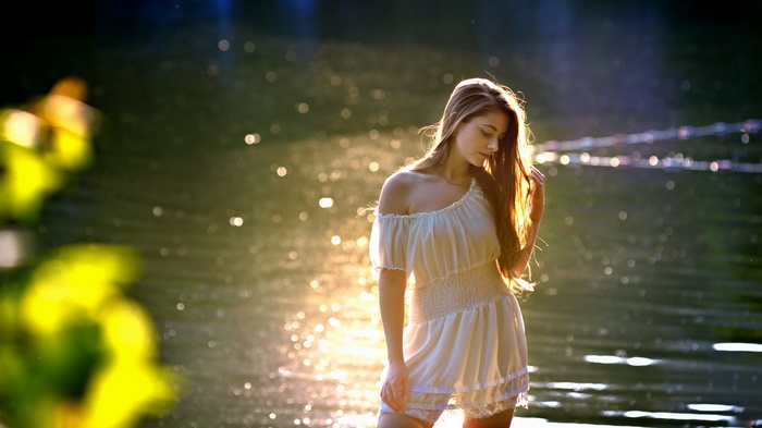 Woman in white dress standing in water at sunset