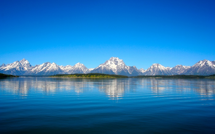 Snow-capped mountains reflected in a clear lake under a blue sky