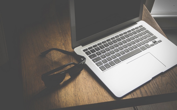 MacBook laptop and glasses on a wooden table