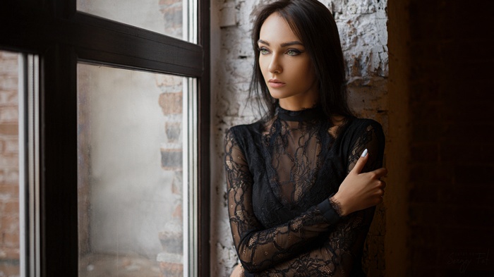 Portrait of a woman in a black lace top by a window