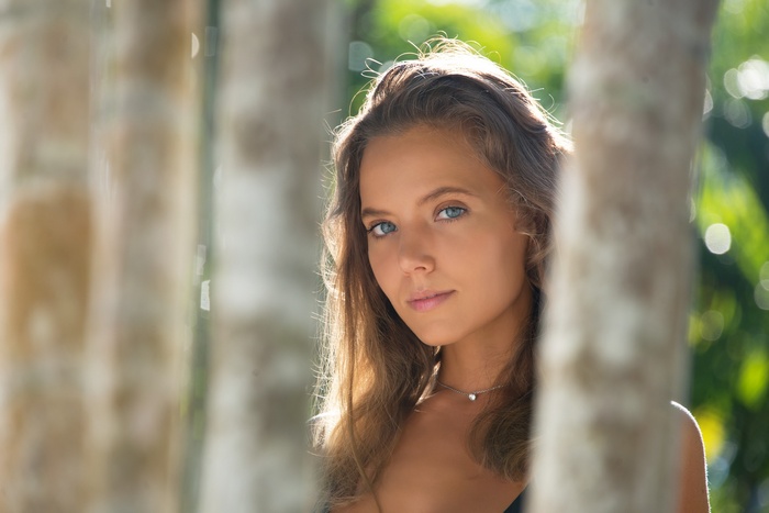 women, Katya Clover, bokeh, brunette, women outdoors, portrait, long hair, bare shoulders, face, trees, model, blue eyes, looking at viewer, necklace