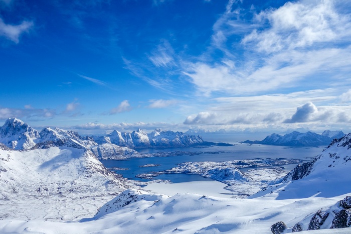 Snowy mountains and a blue bay under a cloudy sky