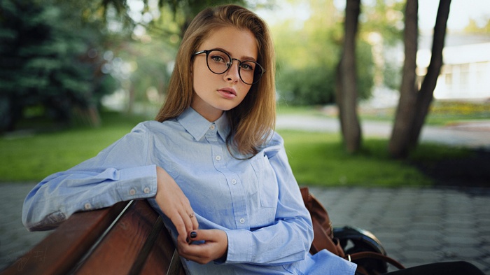 Woman with glasses sitting on a bench in a park