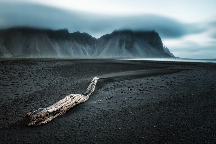 Driftwood on a black sand beach with mountains