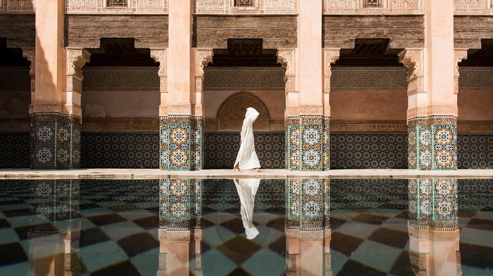 Person in white robe walking by a pool in Marrakesh