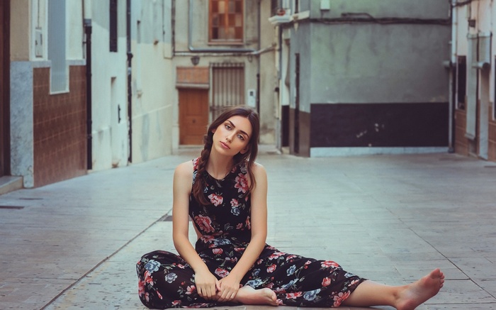Woman in floral dress sitting barefoot in urban alley