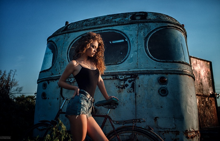 Woman in jean shorts and leotard with bicycle by old car