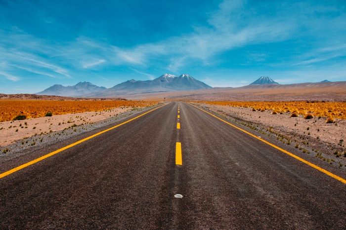 Desert road leading to snow-capped mountains under a blue sky