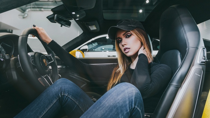 Woman in Porsche wearing baseball cap and jeans
