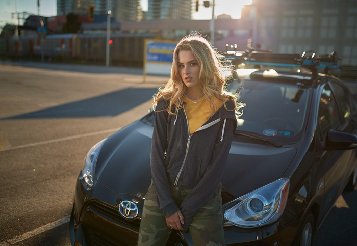Woman in hoodie and camouflage pants leaning on car