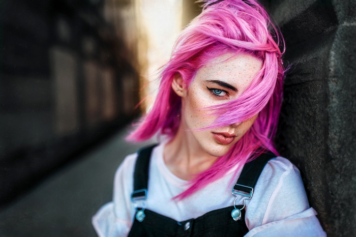 Woman with pink hair and freckles wearing overalls