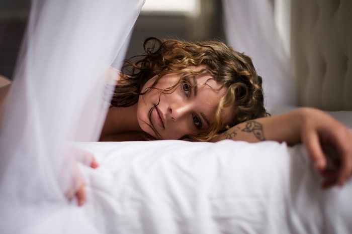 Woman lying in bed with sheer curtains