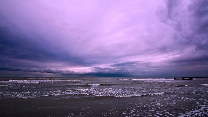 Purple sky over a dark sea with waves and a boat