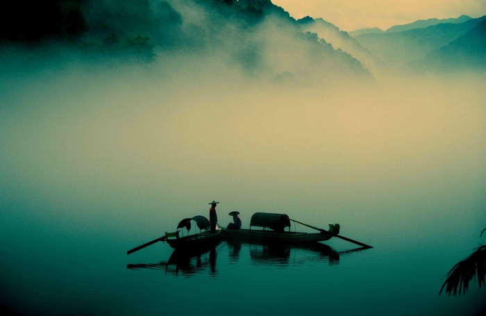 Two canoes on a misty lake with mountains in the background