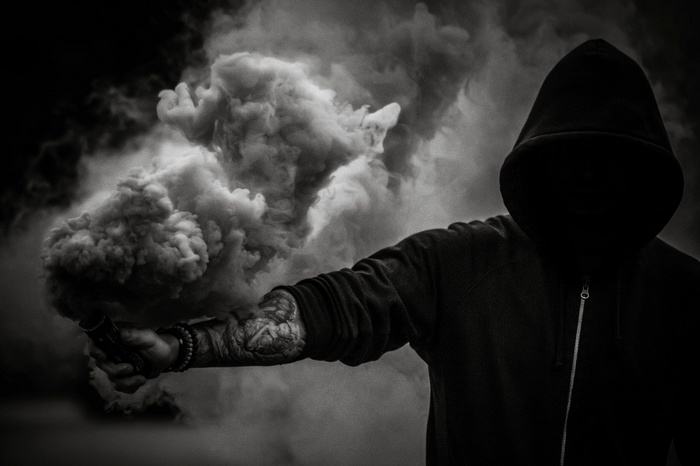 Person in a hood holding a smoke bomb
