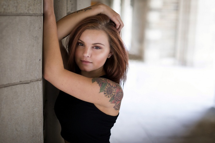 Woman with tattoos leaning against a concrete wall