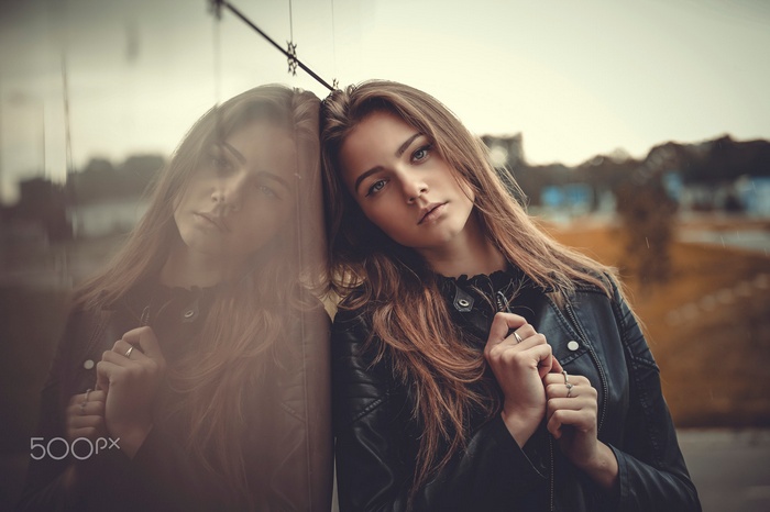 Woman in leather jacket leaning against reflective surface