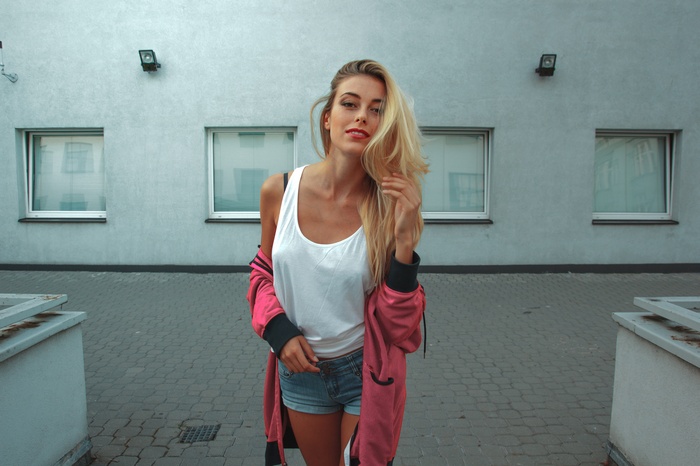 Woman with blonde hair wearing a white tank top and jean shorts