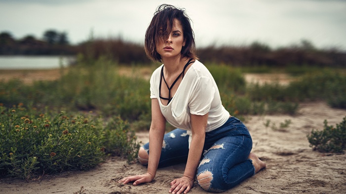 Woman in ripped jeans and white top kneeling outdoors