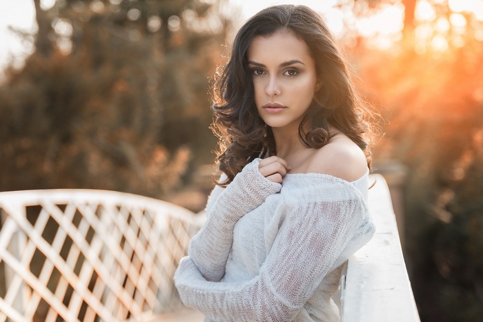Woman in off-the-shoulder sweater on a bridge at sunset