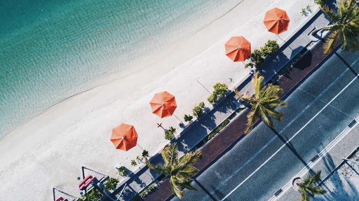 Aerial view of a tropical beach with orange umbrellas and palm trees