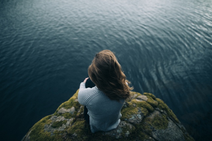 Woman sitting on a mossy rock overlooking the sea