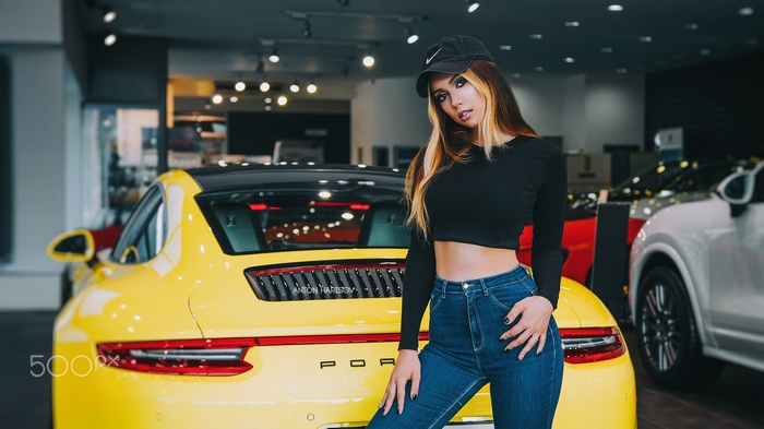 Woman in black crop top and jeans posing by yellow Porsche