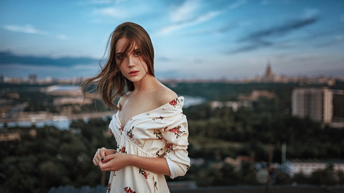 Woman in floral dress on rooftop overlooking cityscape