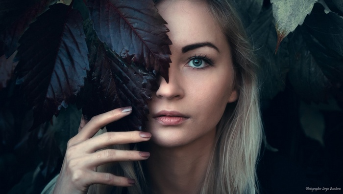Woman with blonde hair and green eyes behind leaves