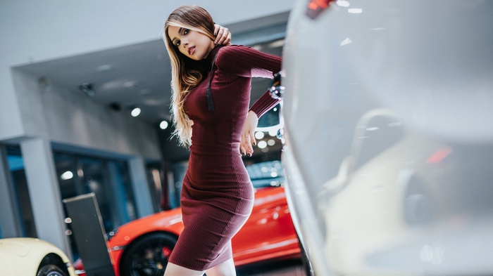 Woman in maroon dress posing near cars