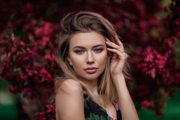 Woman with blonde hair in front of red flowers