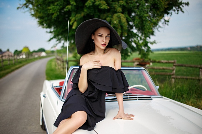 Angelina Petrova in a black dress and hat with a car