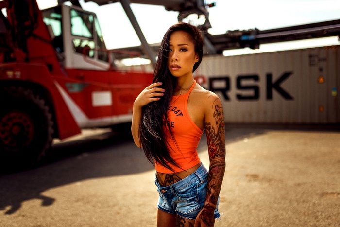 Woman with tattoos in orange halter top and jean shorts