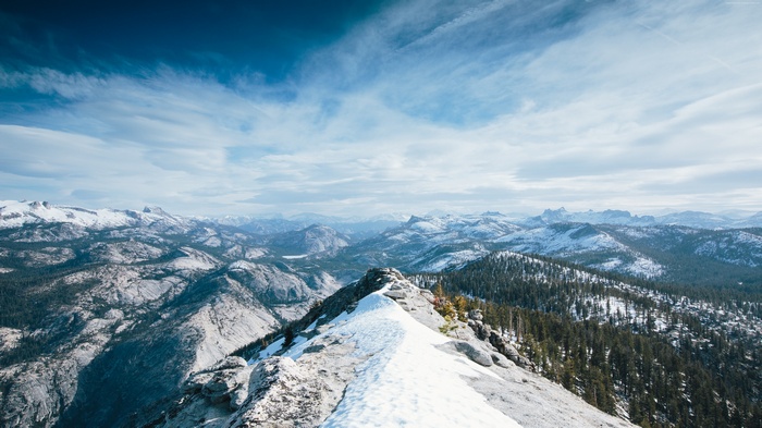 Snowy mountain range with pine trees under a cloudy sky
