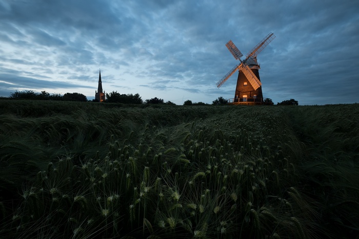 Windmill and church spire in a field at dusk