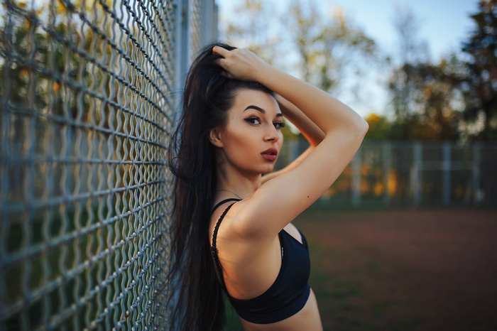 Woman in sports bra leaning against a fence