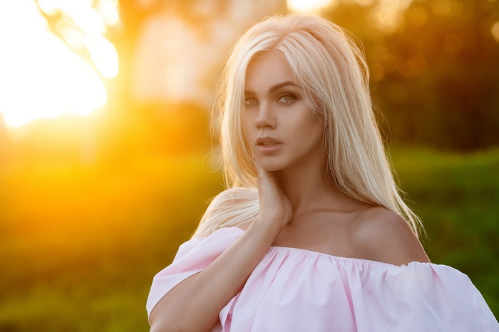 Woman with blonde hair in pink off-the-shoulder top at sunset