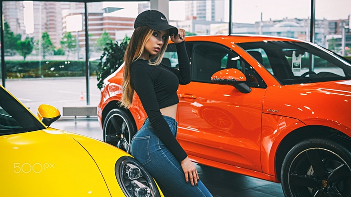 Woman in baseball cap and jeans posing with cars