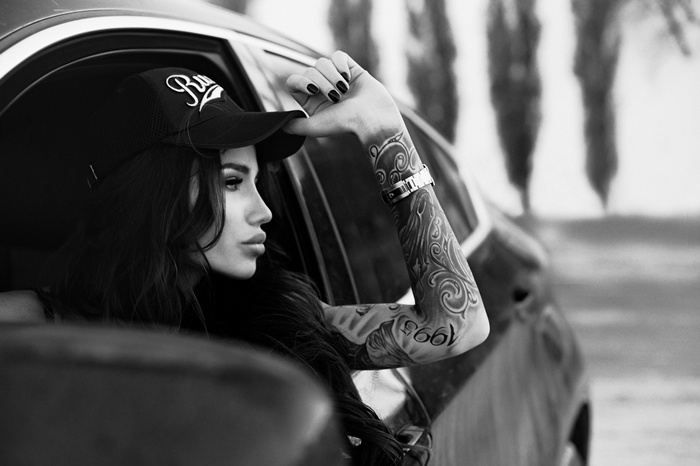 Woman with tattoos and baseball cap in car