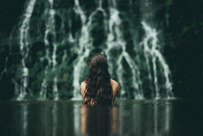 Woman bathing in a river in front of a waterfall