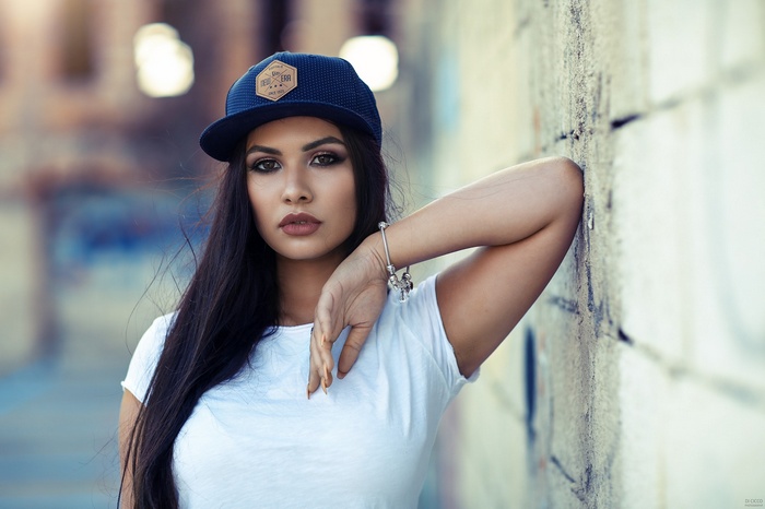 Woman wearing a baseball cap and white t-shirt leaning against a wall