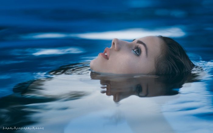 Woman with wet hair floating in blue water