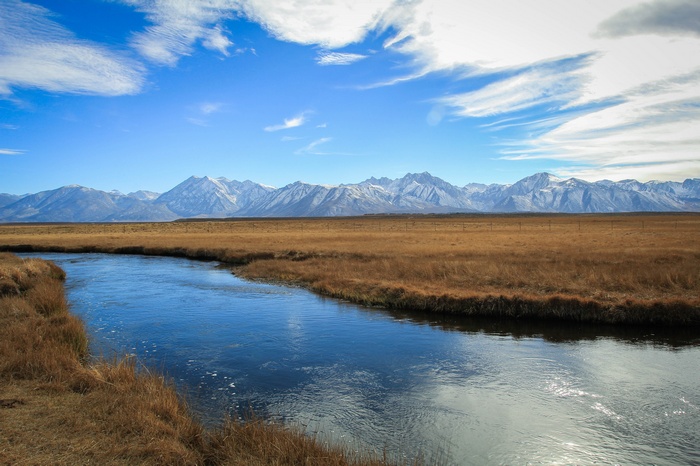 River flowing through a meadow with snow-capped mountains in the background